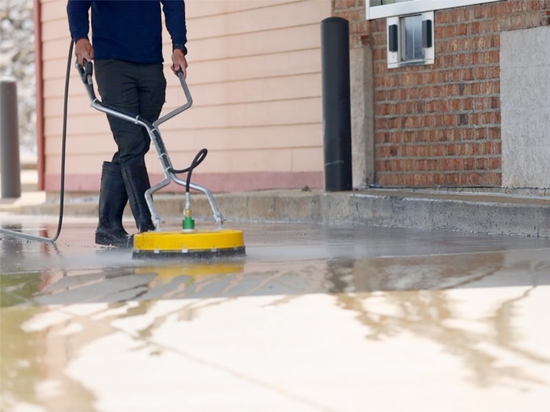 Technician uses powerful rotary pressure washing device to provide residential concrete cleaning