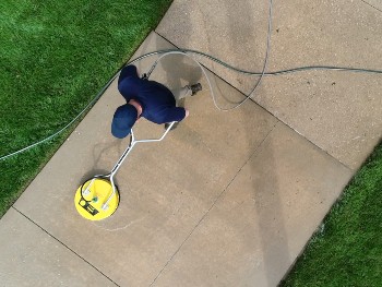 Cleaning staff uses a two-handed rotary pressure washer to clean dirty cement floor